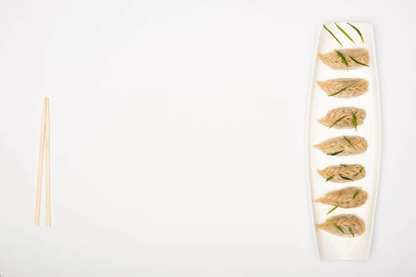Vista dall'alto di deliziosi gnocchi cinesi bolliti sul piatto vicino a bacchette su sfondo bianco — Foto stock
