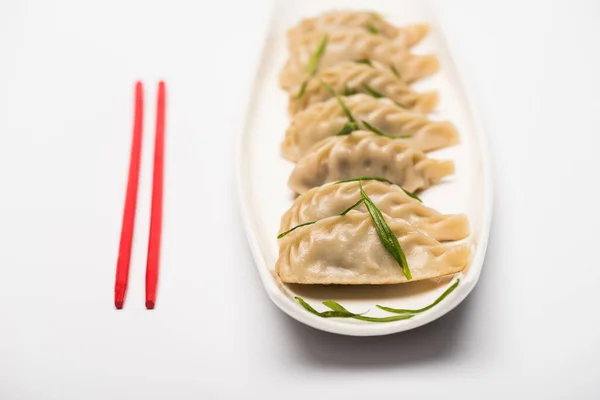 Deliziosi gnocchi cinesi bolliti sul piatto vicino bacchette su sfondo bianco — Foto stock