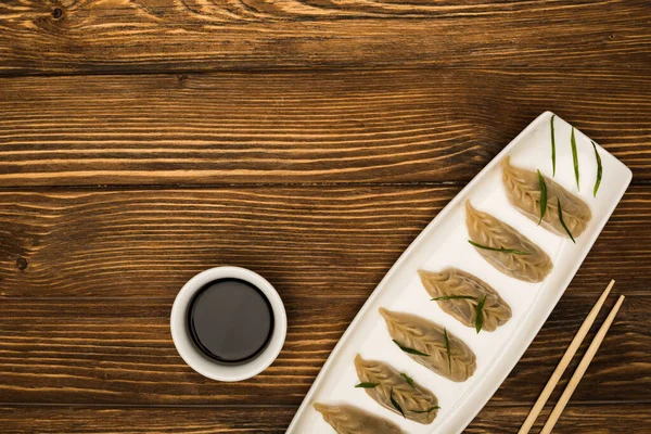 Vue du dessus de délicieuses boulettes bouillies chinoises sur assiette près des baguettes et de la sauce soja sur table en bois — Photo de stock