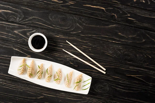 Vista dall'alto di deliziosi gnocchi cinesi bolliti sul piatto vicino a bacchette e salsa di soia sul tavolo di legno nero — Foto stock