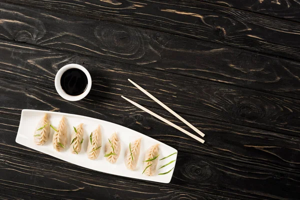 Vista superior de deliciosas albóndigas hervidas chinas en el plato cerca de palillos y salsa de soja en la mesa de madera negra - foto de stock