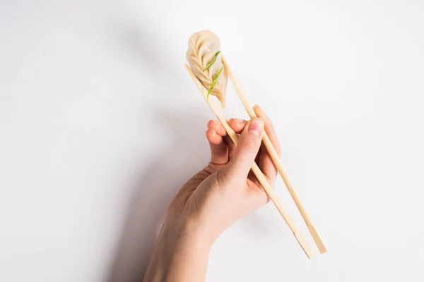 Vista cortada de mulher segurando delicioso bolinho cozido chinês com pauzinhos no fundo branco — Fotografia de Stock