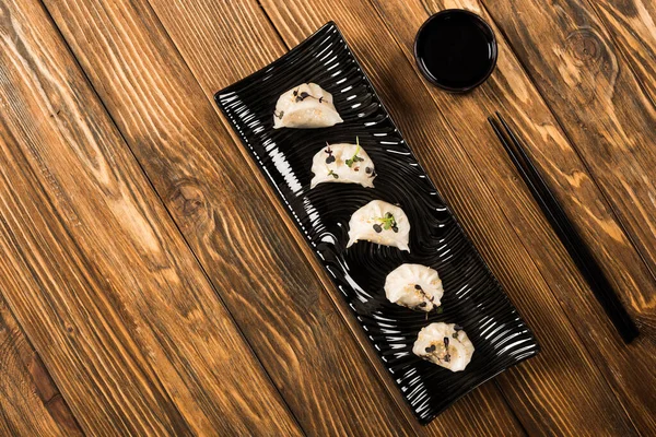 Vue du dessus de délicieuses boulettes bouillies chinoises sur assiette près des baguettes et de la sauce soja sur table en bois — Photo de stock