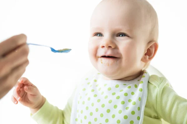 Focus selettivo della madre che alimenta il bambino sorridente isolato sul bianco — Foto stock