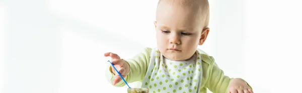 Panoramic shot of infant holding spoon in jar of vegetable baby nutrition on white background — Stock Photo