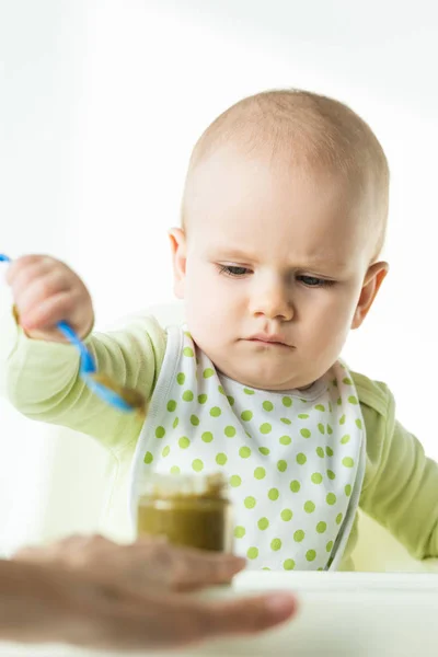 Concentration sélective de la cuillère de bébé près du bocal avec purée de légumes et la mère sur fond blanc — Photo de stock