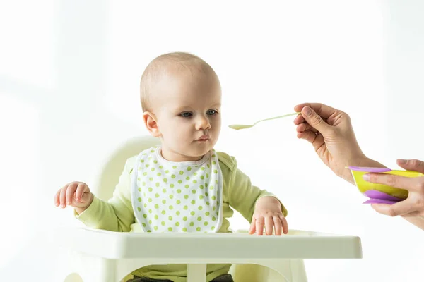 Мать кормит младенца детским питанием на кормящем стуле на белом фоне — стоковое фото