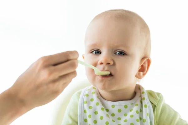 Selective focus of mother with spoon feeding baby with puree on feeding chair isolated on white — Stock Photo
