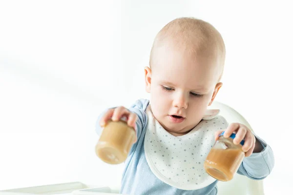 Selective focus of infant on feeding chair holding jars of fruit baby nutrition on white background — Stock Photo