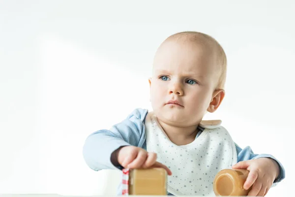 Enfoque selectivo del bebé sosteniendo frascos de puré de frutas y mirando hacia otro lado sobre fondo blanco - foto de stock