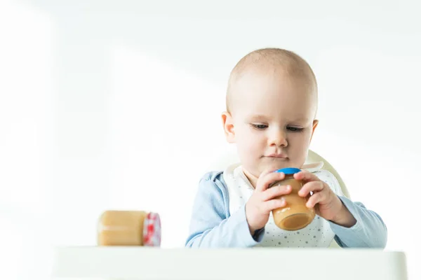 Селективный фокус милого младенца с банками детского питания на столе кормления стулом на белом фоне — стоковое фото