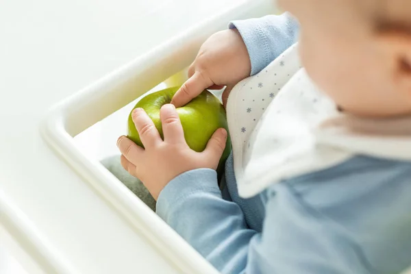 Focus selettivo del bambino che tocca la mela verde sulla sedia di alimentazione isolata su bianco — Foto stock
