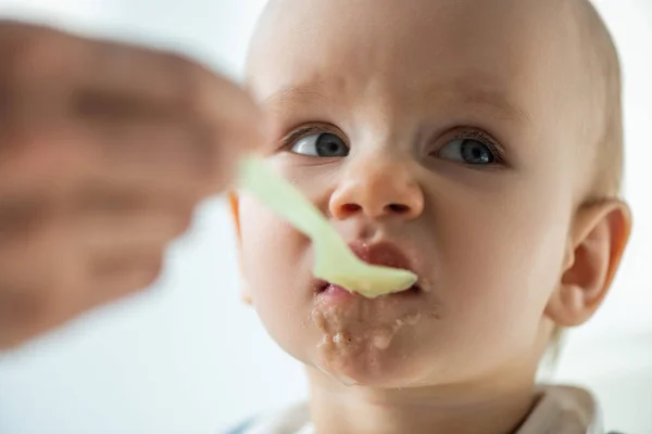 Focus selettivo del bambino che allatta la madre con purea su sfondo grigio — Foto stock