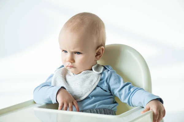 Pensive baby boy sitting on feeding chair on white background — Stock Photo