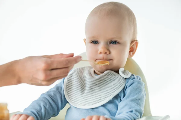 Вибірковий фокус мами, що годує чарівного хлопчика з фруктовим дитячим харчуванням ізольовано на білому — стокове фото