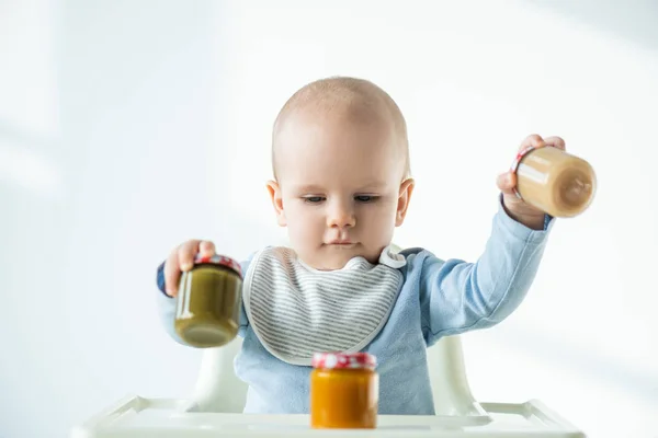 Concentration sélective des pots de maintien de bébé de légumes nutrition bébé tout en étant assis sur la chaise d'alimentation sur fond blanc — Photo de stock