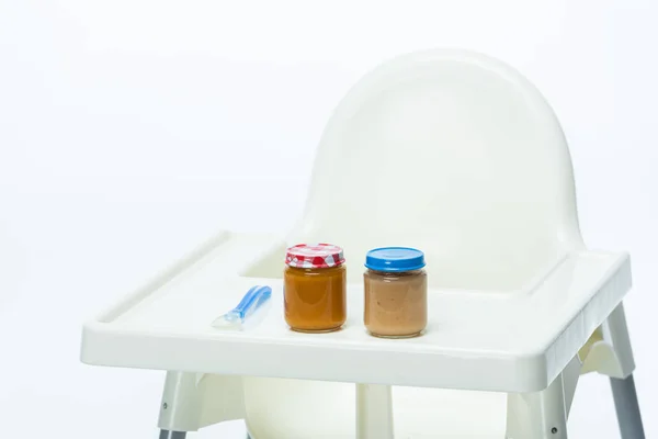 Gläser mit Babynahrung und Löffel auf dem Tisch des Fütterungsstuhls isoliert auf weiß — Stockfoto