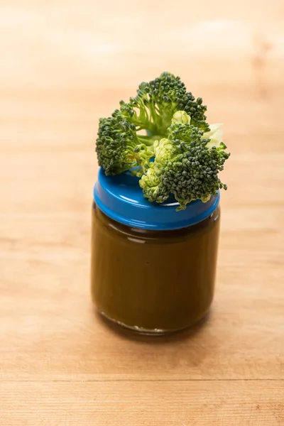 Close up view of piece of broccoli on jar of vegetable baby food on wooden surface — Stock Photo