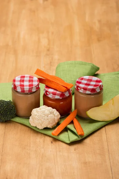 Jars of baby food with cauliflower, broccoli and carrot on napkin on wooden surface — Stock Photo