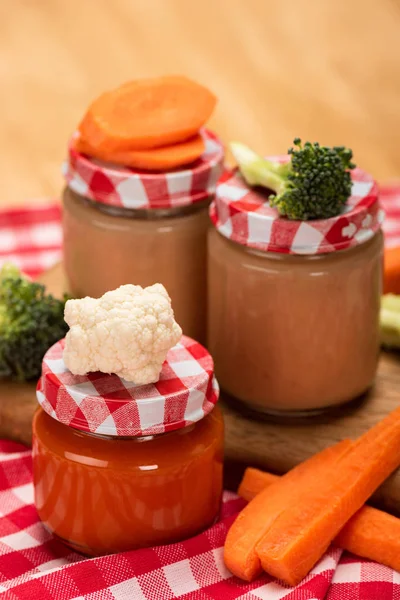 Vista de cerca de la comida para bebés en frascos con verduras frescas en mantel sobre fondo de madera - foto de stock