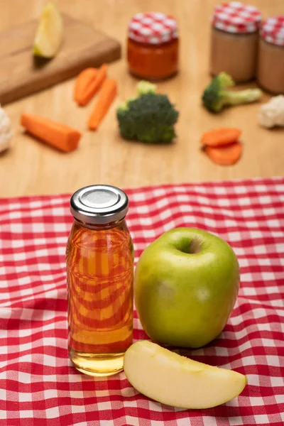 Selective focus of bottle with apple juice and jars of baby food with ingredients on tablecloth on wooden surface — Stock Photo