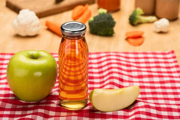 Selective focus of bottle of apple juice and baby food in jars with ingredients on tablecloth on wooden background — Stock Photo