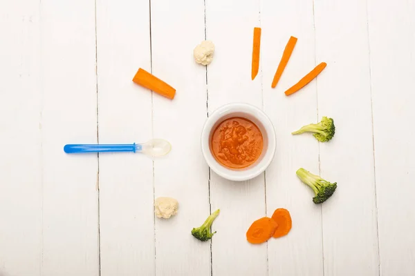 Vista dall'alto della nutrizione del bambino vegetale in ciotola con pezzi di verdure fresche e cucchiaio su una superficie di legno bianca — Foto stock