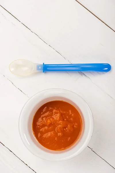 Vue du dessus du bol avec purée de bébé de carotte et cuillère sur fond blanc en bois — Photo de stock