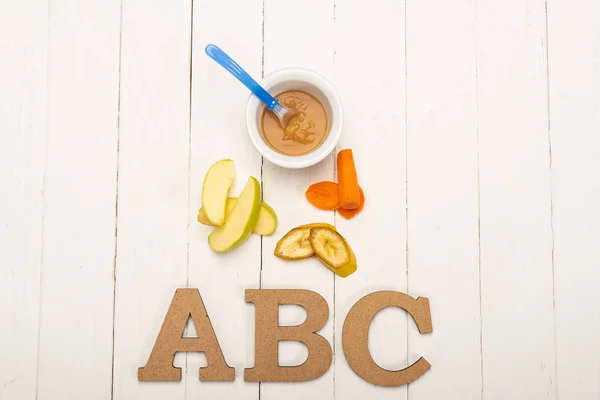 Vue du dessus des ingrédients frais près des aliments pour bébés et des lettres en bois sur une surface en bois blanc — Photo de stock