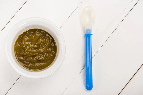 Top view of bowl with baby nutrition and spoon on white wooden background — Stock Photo