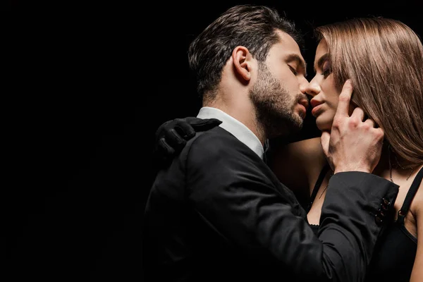 Side view of handsome man in suit kissing attractive woman isolated on black — Stock Photo