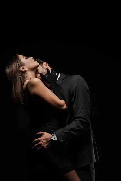 Homem barbudo beijando mulher atraente isolado no preto — Fotografia de Stock