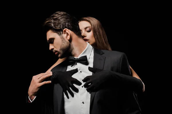 Attractive woman in gloves hugging handsome man in suit isolated on black — Stock Photo