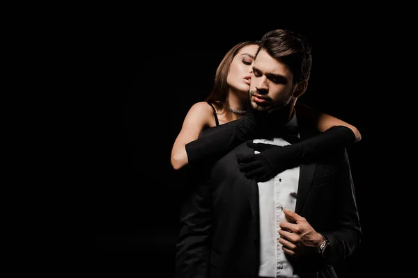 Young woman in gloves hugging handsome man in suit isolated on black — Stock Photo