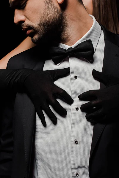 Joven mujer en guantes abrazando hombre en traje aislado en negro - foto de stock