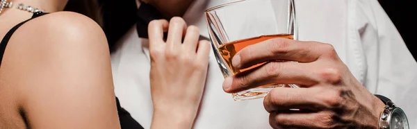 Panoramic shot of woman touching man with glass of whiskey isolated on black — Stock Photo