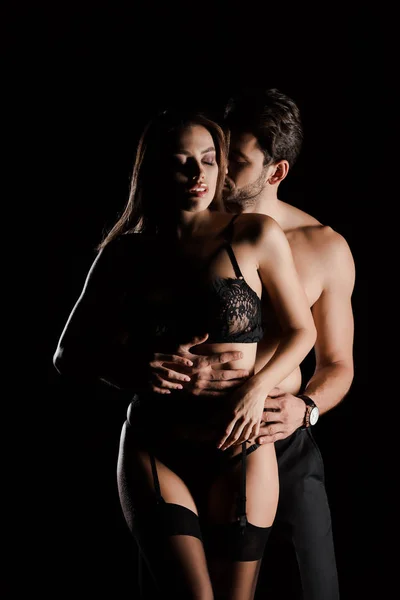 Homme passionné étreignant femme attrayante en dentelle sous-vêtements isolés sur noir — Photo de stock