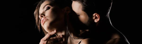 Панорамний знімок чоловіка цілує спокусливу жінку із закритими очима ізольовано на чорному — стокове фото