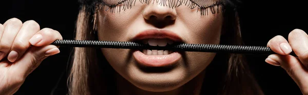 Tiro panorâmico de mulher segurando chicote açoitamento na boca isolado no preto — Fotografia de Stock