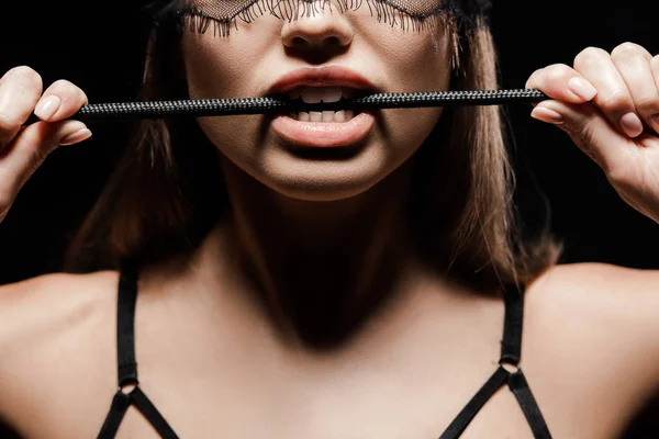 Cropped view of seductive woman holding flogging whip in mouth isolated on black — Stock Photo