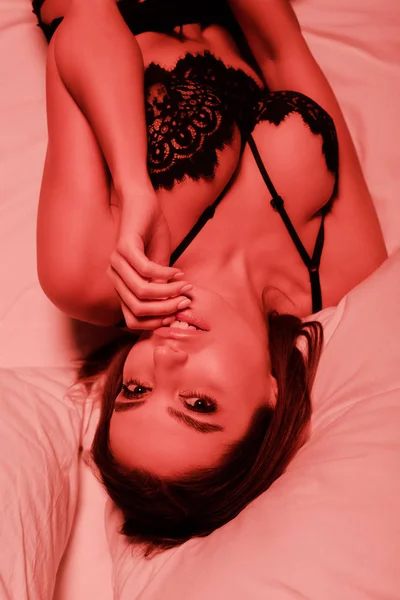 Vista superior de la mujer sexy tocando los labios mientras está acostado en la cama - foto de stock
