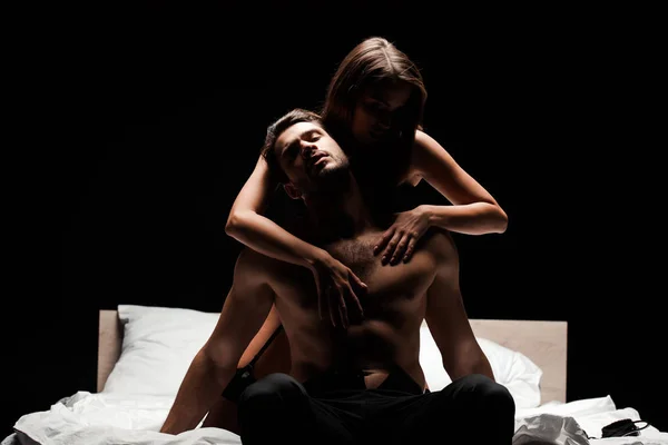 Страстная женщина трогает мужчину без рубашки на кровати, изолированного от черного — стоковое фото