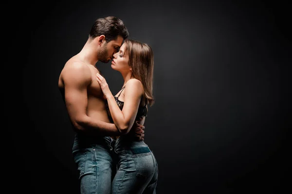 Vue latérale de musclé homme baisers séduisante fille sur noir — Photo de stock