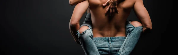 Plan panoramique de l'homme musclé tenant dans les bras fille en jeans sur noir — Photo de stock