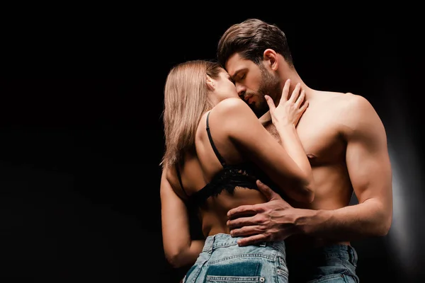 Shirtless man with closed eyes kissing woman in jeans on black — Stock Photo