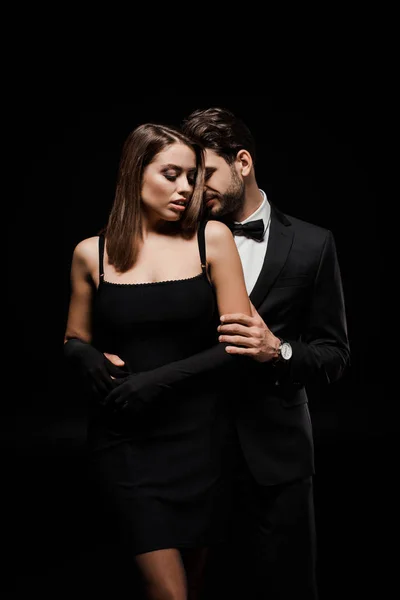 Homme en tenue formelle étreignant belle femme dans des gants isolés sur noir — Photo de stock