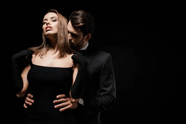 Handsome man in suit hugging attractive woman with closed eyes isolated on black — Stock Photo