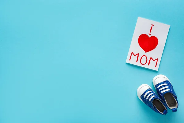 Top view of greeting card with i love mom lettering near baby booties on blue background — Stock Photo