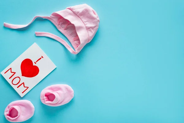 Top view of greeting card with i love mom lettering near baby clothes on blue background — Stock Photo