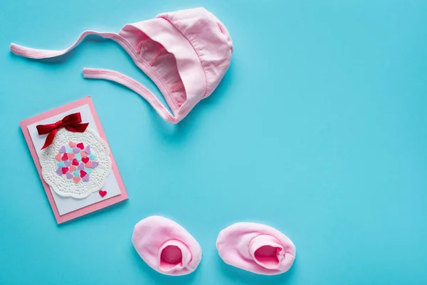 Vue du dessus des vêtements de bébé rose et carte de vœux sur fond bleu, concept de fête des mères — Photo de stock